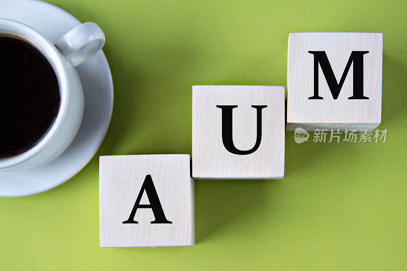 AUM -首字母缩略词木制大立方体在绿色背景与一杯咖啡